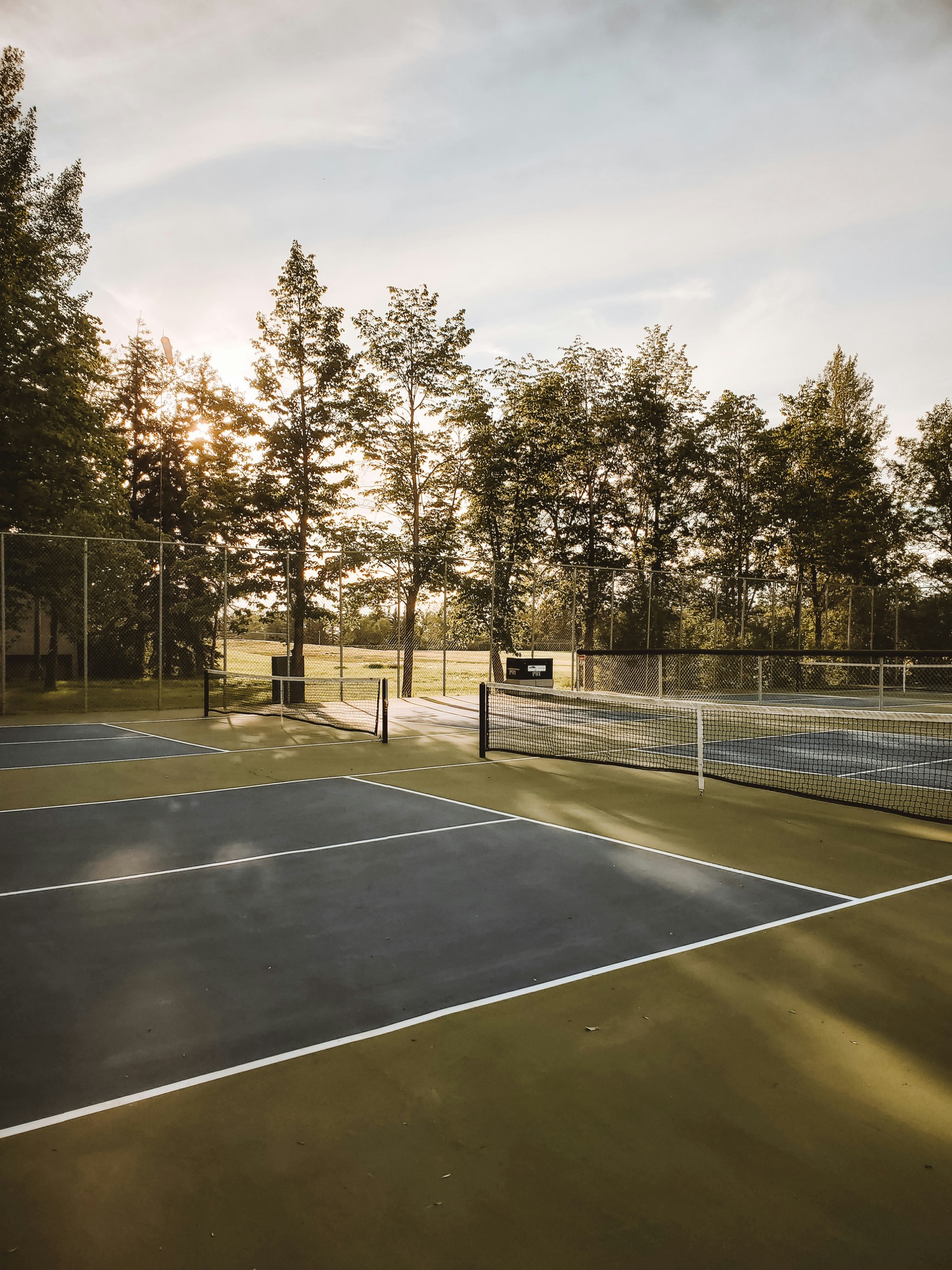 Tennis court with sunlight streaming through trees in background by Angela Bailey on Unsplash.