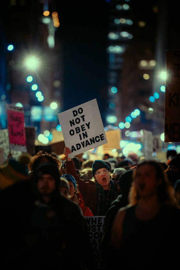 Protester holding up a sign "Do Not Obey In Advance." Photo by Colin Lloyd/Unsplash